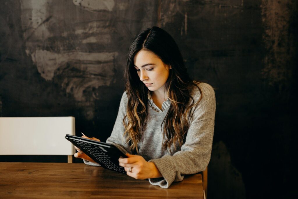 A woman in a grey sweater using a tablet at a wooden table
